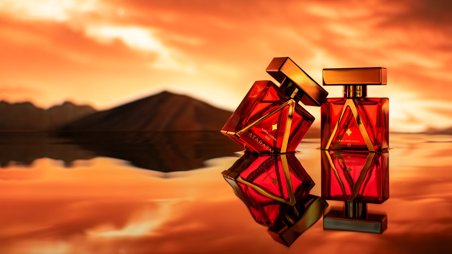 Two red and gold Kama Collection perfume bottles with a mountain and sunset reflection in the background